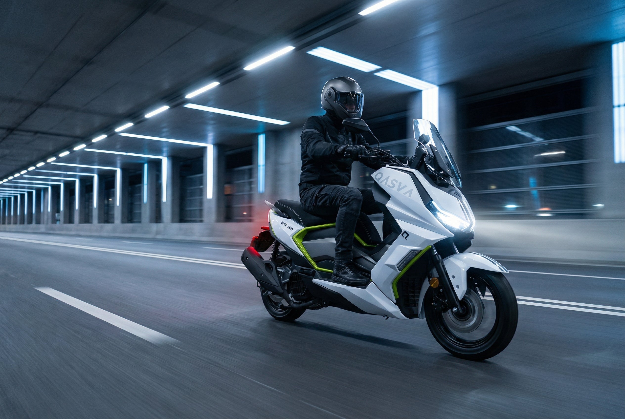 Fahrer auf einem weißen Motorroller bei Nacht auf einer beleuchteten Stadtstraße